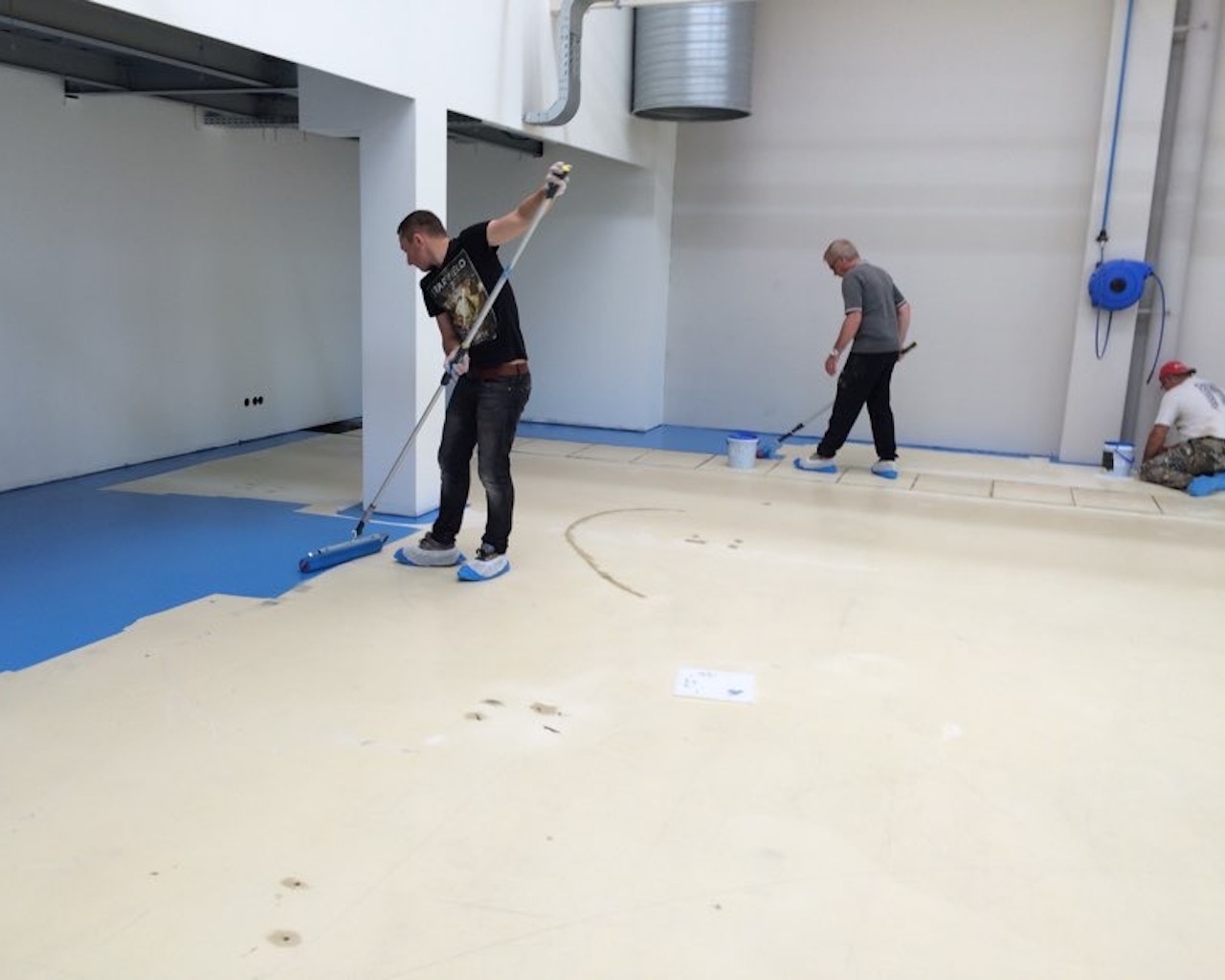 L'équipe applique la première couche de PU color ESD bleu avec des rouleaux à peinture. Les employés sont équipés de sur-chaussures.