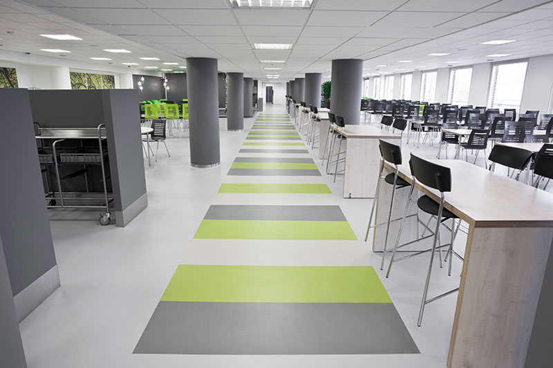 Un réfectoire rénové avec les produits Dr. Schutz. Un sol dans un gris clair avec des bandes de gris plus foncé et vertes claires. Colones grises foncées.