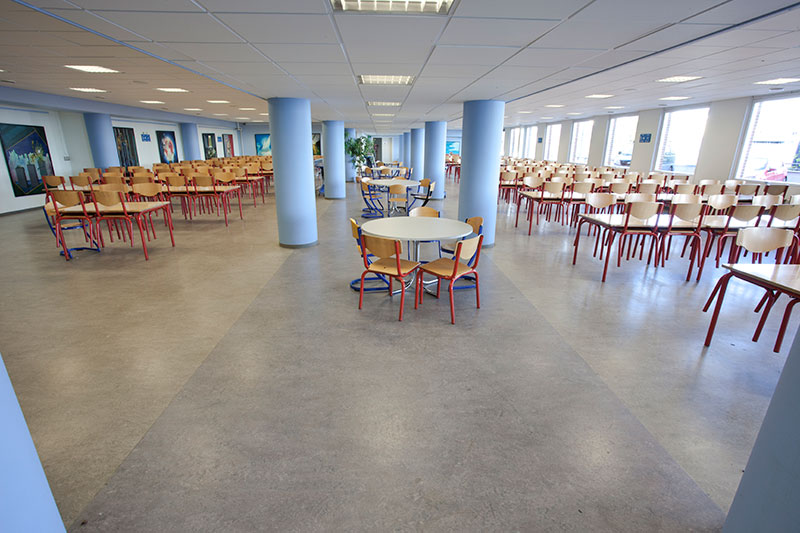 Un réfectoire avant sa rénovation. Sol dans les tons gris/beige. Colones bleues.