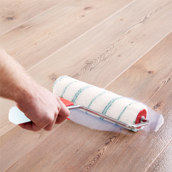 Un rouleau dépose du PU sur un sol stratifié.