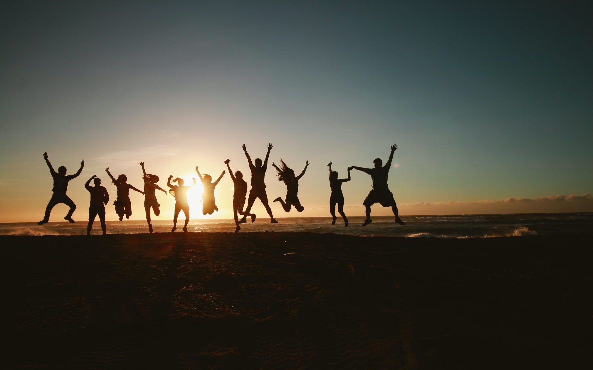 groupe de personnes qui sautent sur la plage au soleil couchant